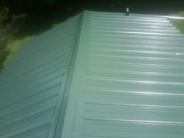 New green metal panels meeting at the ridge of a roof — Flat Roof Repair work by our crew in Clinton