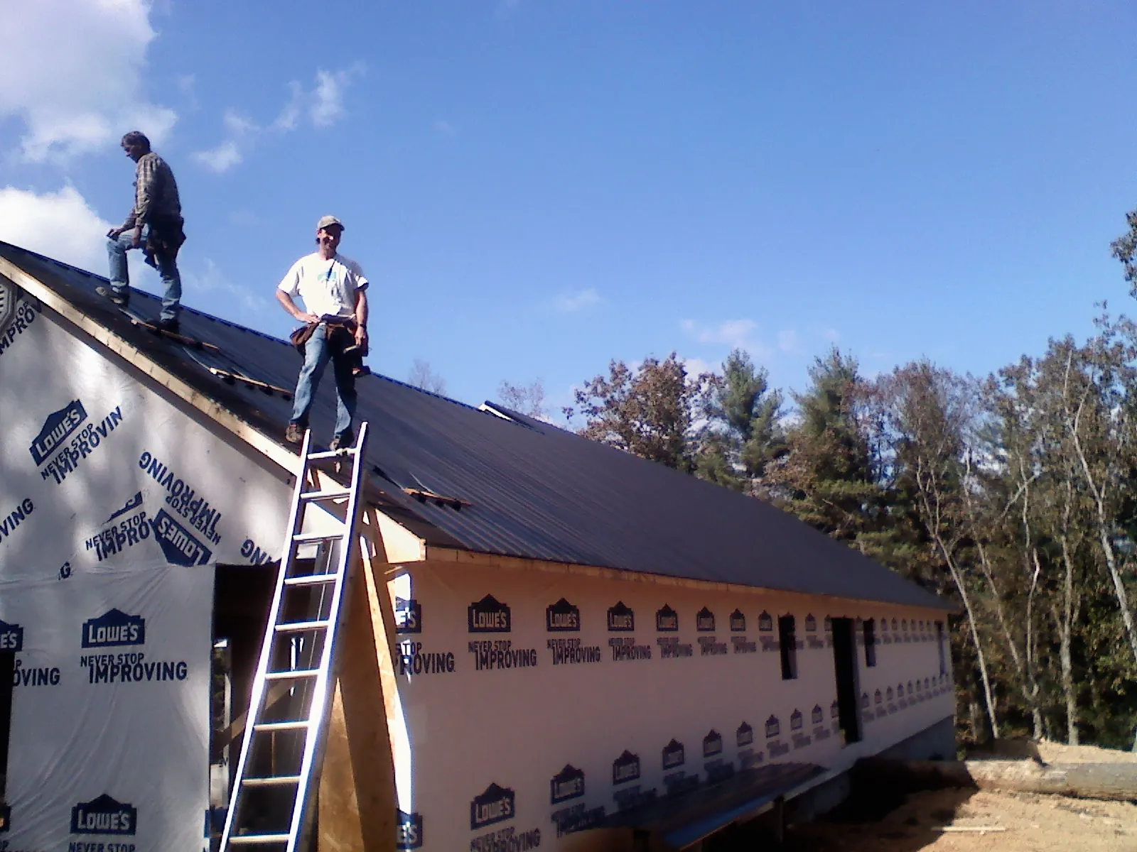 Two roofers standing on a long dark metal roof over a wrapped building in Clinton